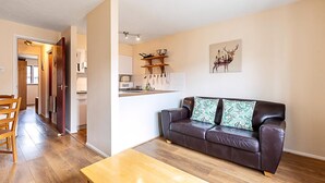 Una sala de estar con un sofá de cuero, una mesa de centro de madera y una cocina al fondo.