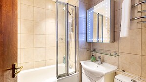 Un baño moderno con ducha de vidrio, lavamanos blanco y espejo con iluminación.