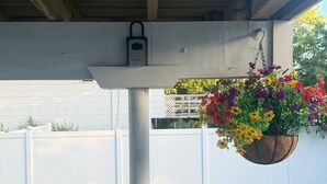A hanging flower basket under a covered patio area with a white fence in the background. - Cozy 1-Bedroom Apartment in Peaceful Commack with Air Conditioning & C. Monoxide (Commack)