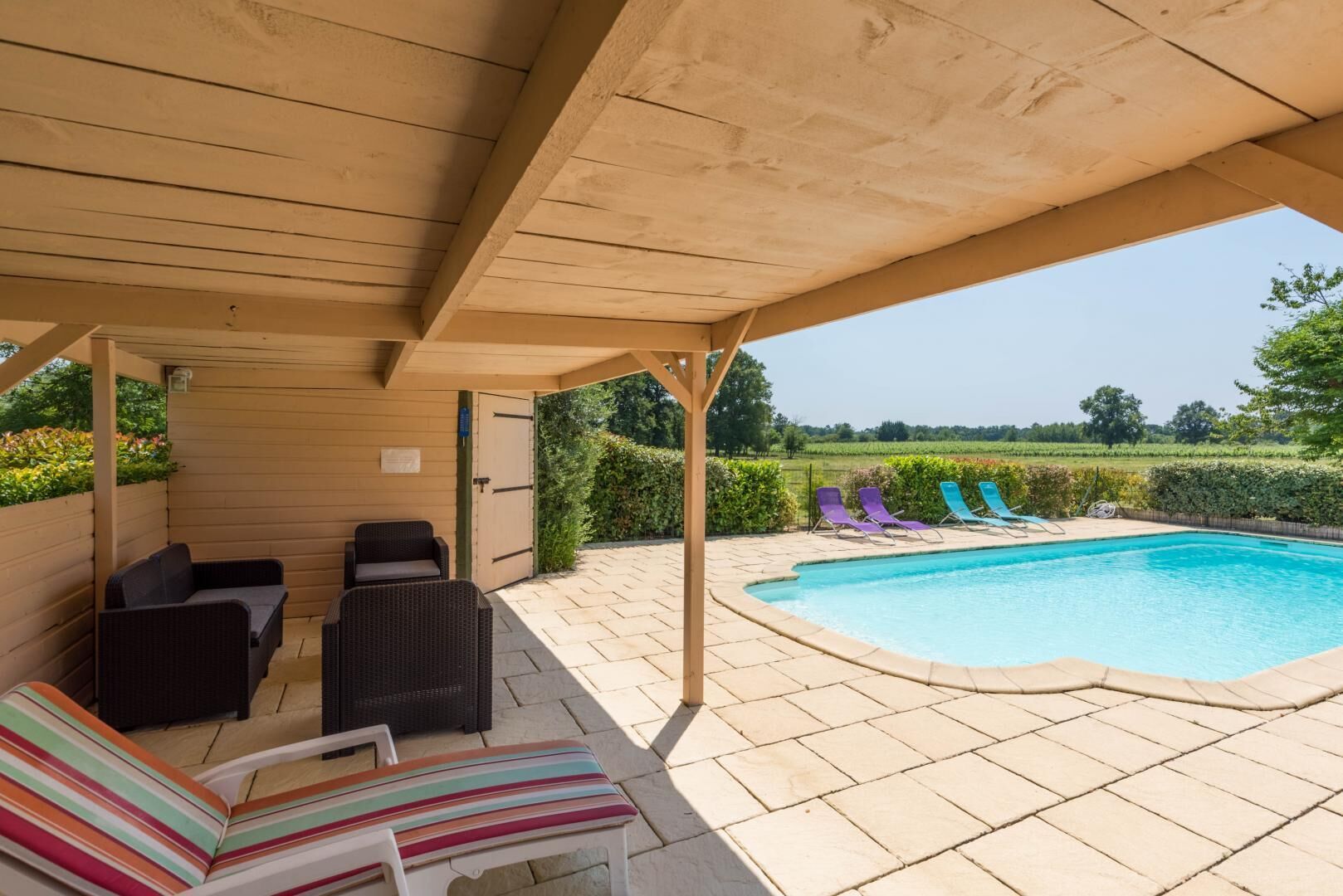 A covered outdoor area with a pool, lounge chairs, and a view of the countryside.