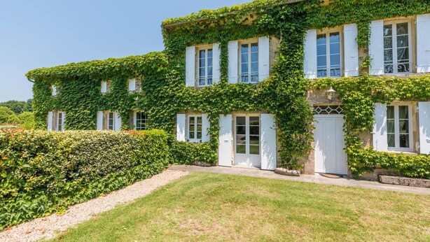 Un grand bâtiment recouvert de lierre, doté de nombreuses fenêtres et portes, et entouré d’une pelouse bien entretenue et de haies.