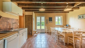 Une cuisine avec un coin repas, des poutres apparentes en bois au plafond et une vue sur l’extérieur.
