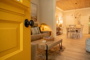 A yellow door with a black handle, a sofa with a patterned throw, a wooden coffee table, and a dining area with a chandelier. - Laid-back, luxurious 4-bed, 2-bath home, 10-minute walk to downtown Saugatuck (Saugatuck)