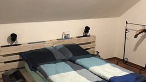 A bed with a wooden headboard, a blue and white bedspread, and a metal rack with clothes. - Find peace and discover yourself (Hürtgenwald)