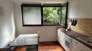 A compact kitchen with a dining table, a window with a view of greenery, white cabinets, and a tiled floor. - Find peace and discover yourself (Hürtgenwald)