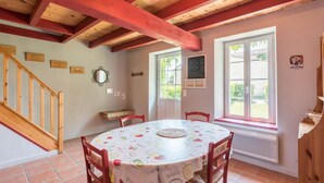 A dining area with a round table, chairs, a wooden staircase, and a window with a view. - Petit Gite de la Mondette (LES-SALLES-DE-CASTILLON)