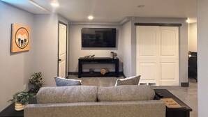Una sala de estar con un sofá, un televisor, una consola y una puerta.