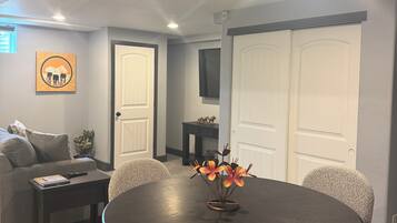 A dining area with a round table, six chairs, a vase with flowers, a sofa, a coffee table, and a TV on the wall.