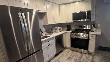 A modern kitchen with stainless steel appliances, white cabinetry, and a herringbone-patterned floor.