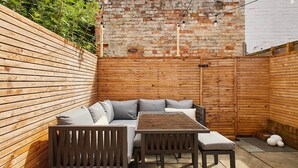 A wooden deck with a sofa and table, brick wall, and a wooden fence. - Host Stay Belvedere Terrace (Scarborough)