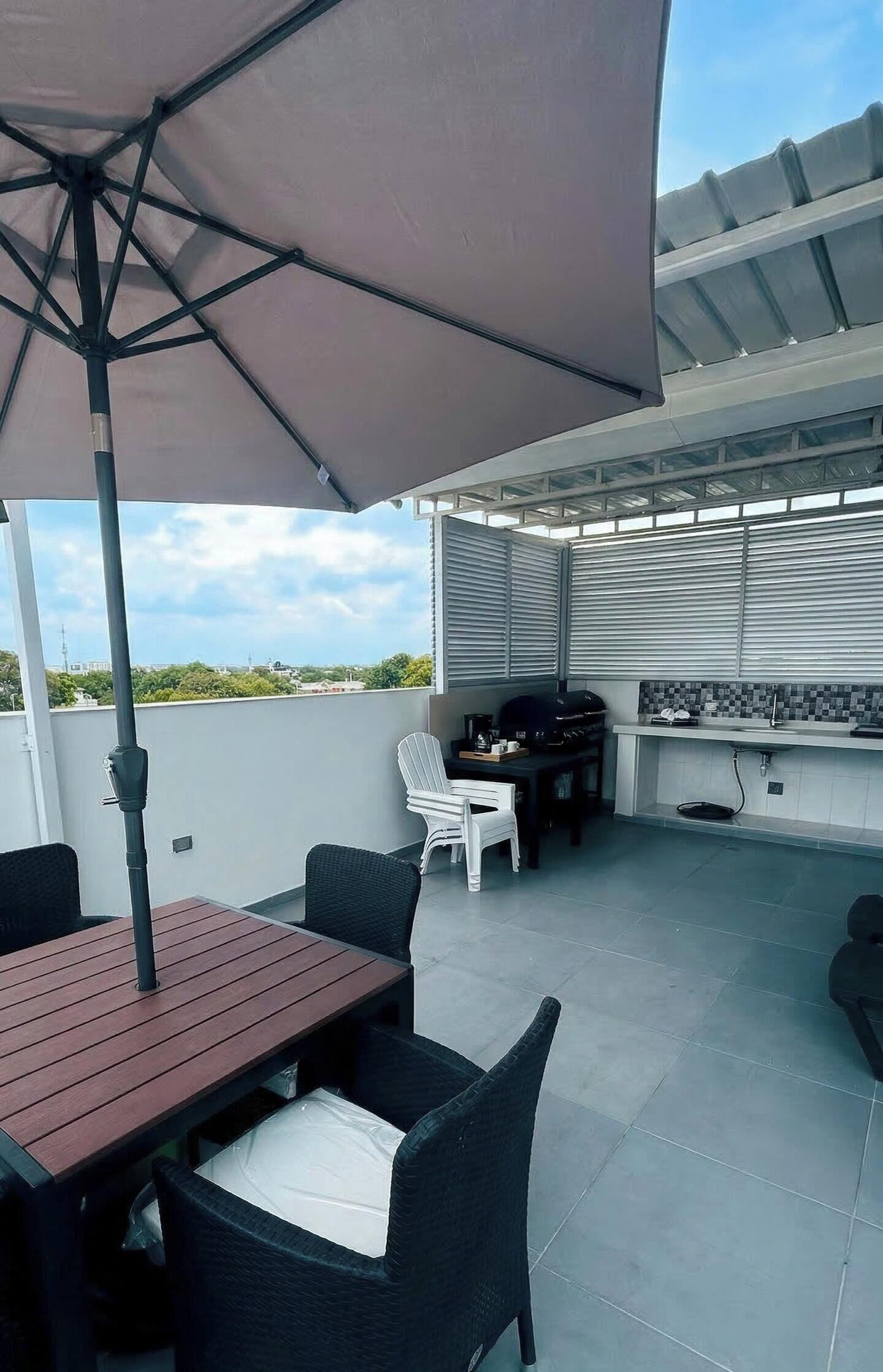 Un patio al aire libre con mesa y sillas, una parrilla y un gran paraguas.
