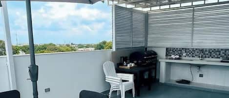 An outdoor patio with a table and chairs, a grill, and a large umbrella.