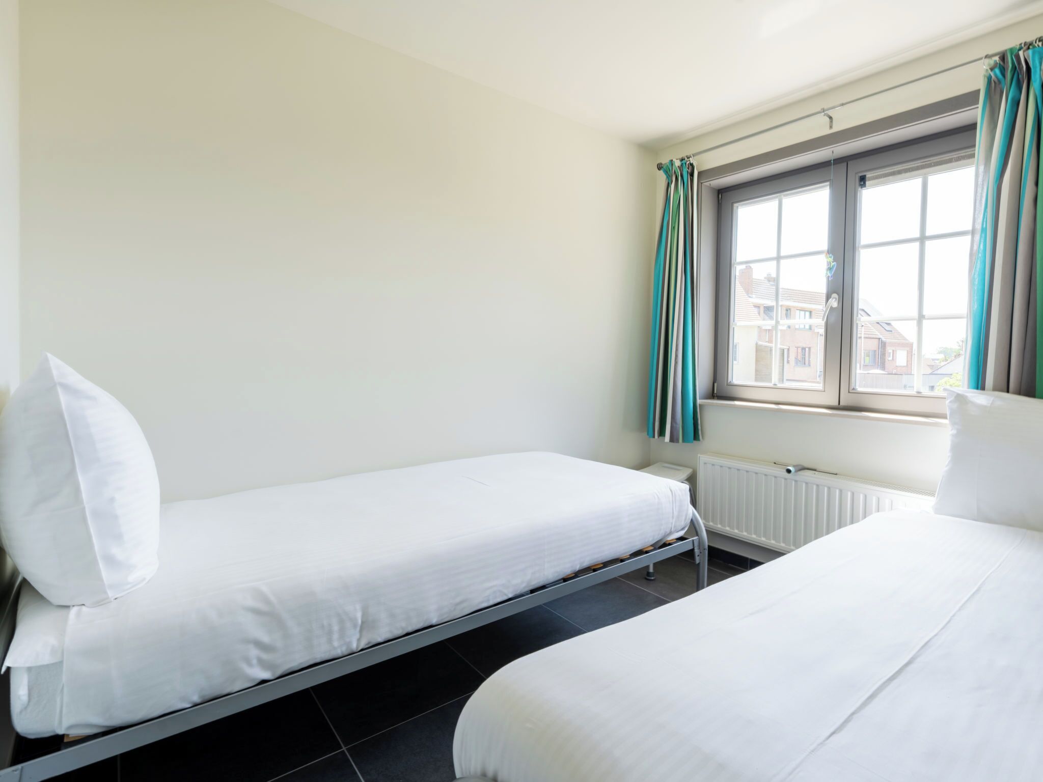 A room with two single beds, a window with curtains, and a radiator.