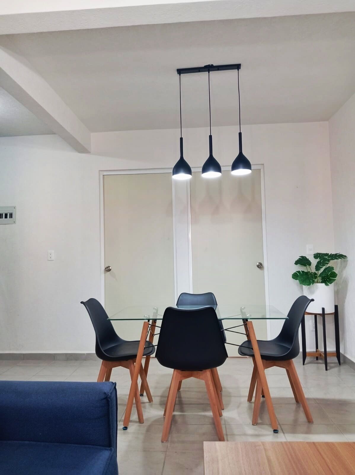 A modern dining area with a glass table, black chairs, and pendant lighting.