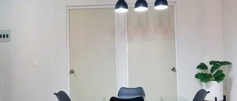 A modern dining area with a glass table, black chairs, and pendant lighting.