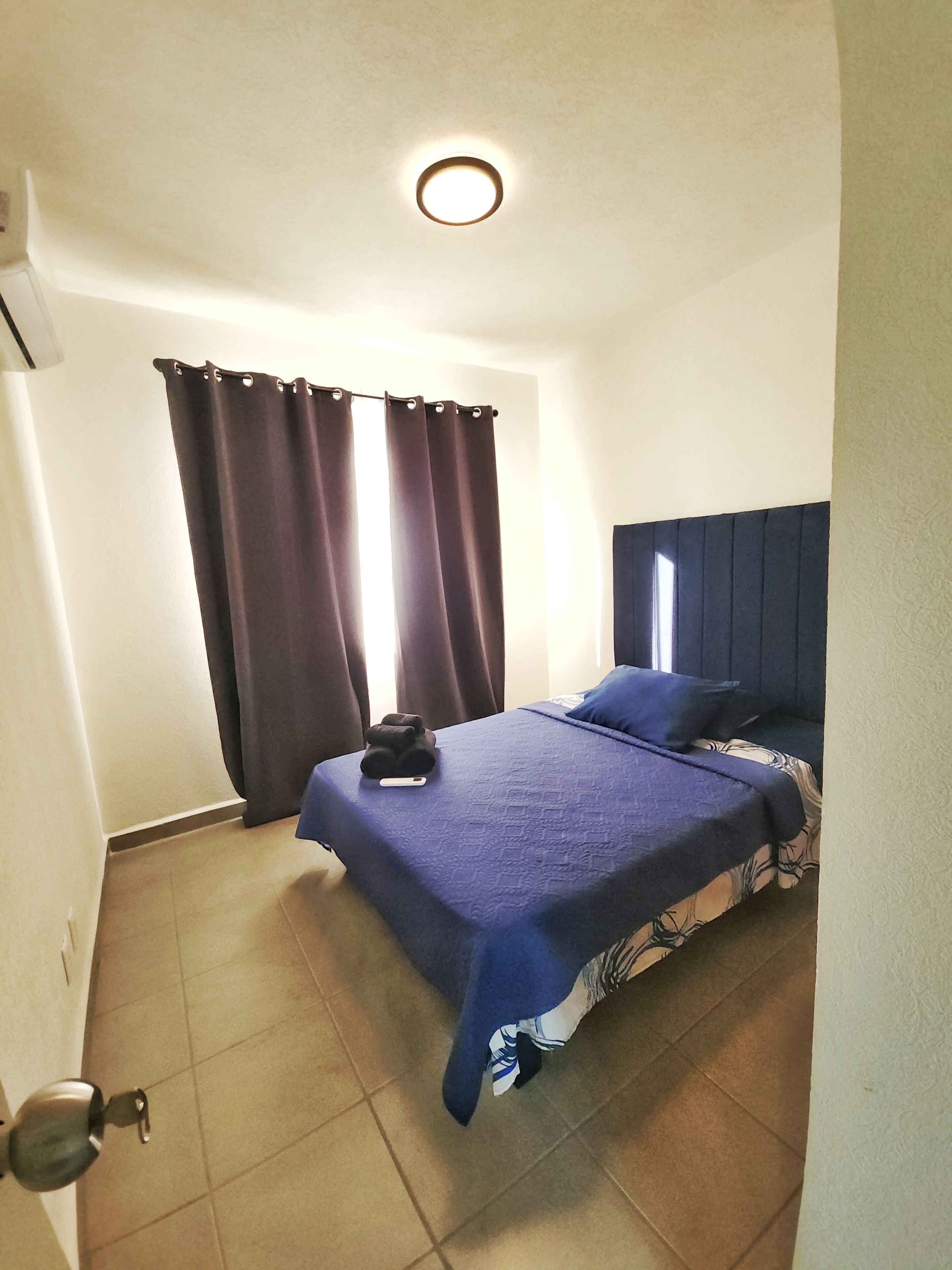 Une chambre à coucher avec un lit, des rideaux, une tête de lit et un luminaire au plafond.