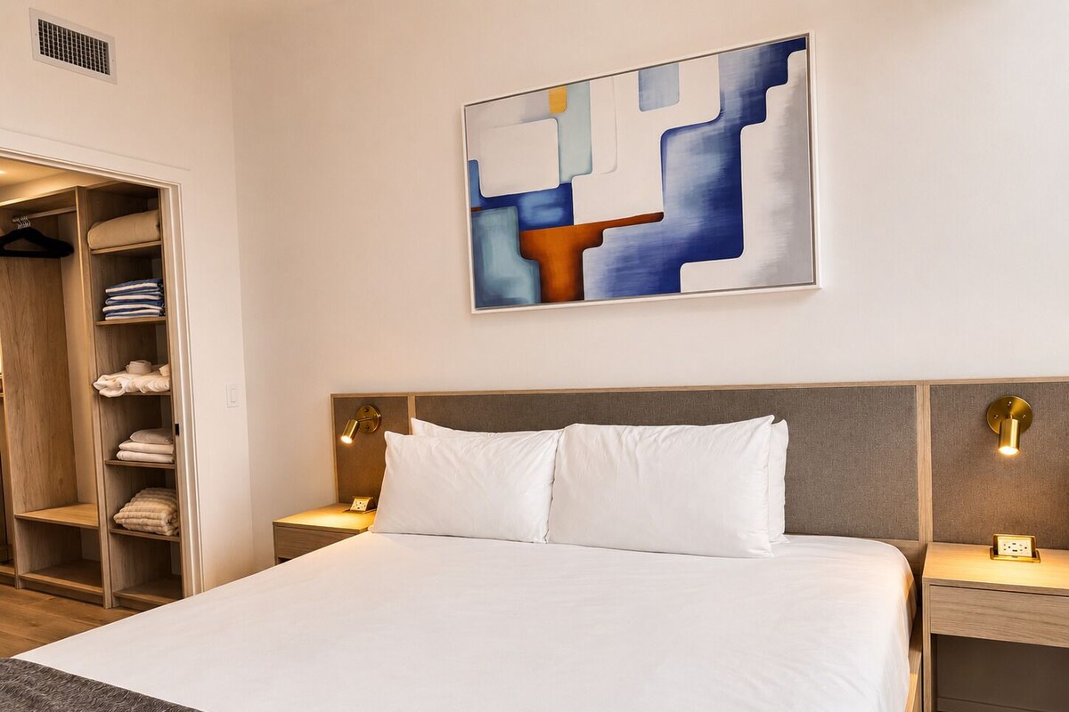 A hotel room with a bed, bedside tables, a wardrobe, and a painting on the wall.