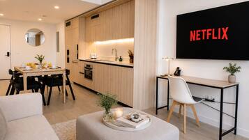 Ein modernes Wohnzimmer mit Essbereich, Küchenzeile und einem an der Wand befestigten Fernseher, der 'NETFLIX' anzeigt.
