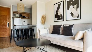 Ein Wohnzimmer mit einer Couch, einem Couchtisch, einer Küchenzeile mit Barhocker und abstrakter Kunst an der Wand.