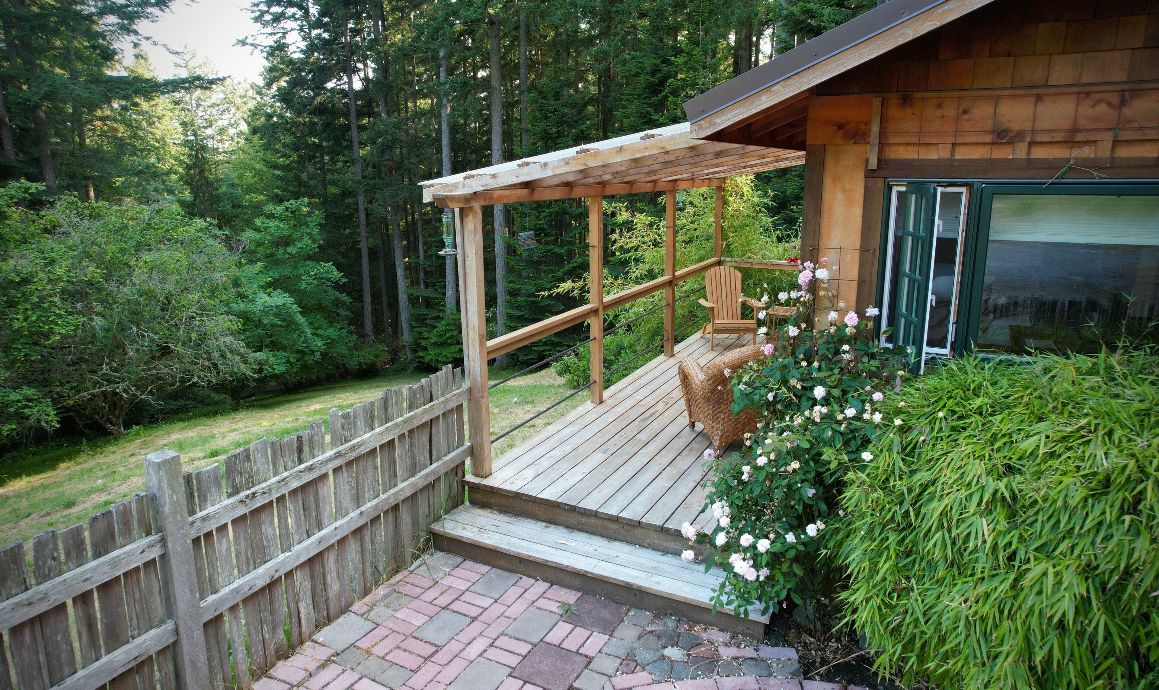 A wooden deck with a pergola, a wicker chair, and a rose bush.