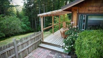 A wooden deck with a pergola, a wicker chair, and a rose bush.