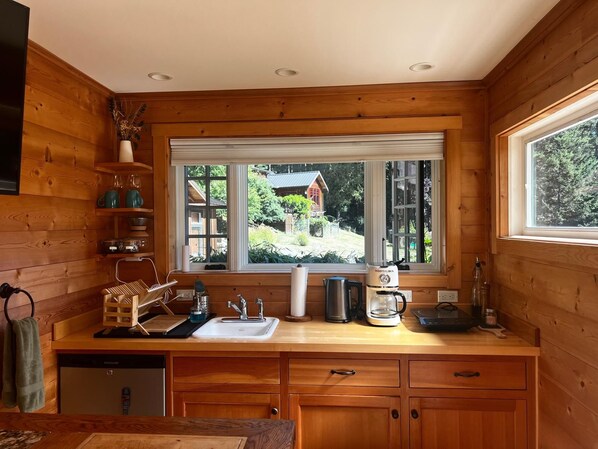 Cocina de cabaña de madera con vistas al exterior, un lavabo, una cafetera y armarios de madera.