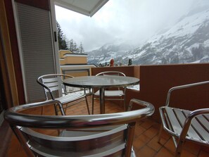 Ein Balkon mit rundem Tisch und Metallstühlen, mit Blick auf einen verschneiten Berg.