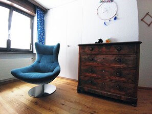 Une pièce avec une chaise bleue, une commode en bois et une fenêtre ornée de rideaux bleus.