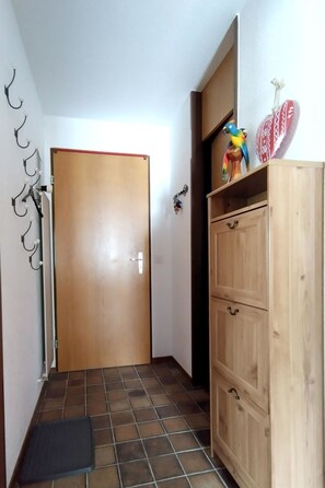Ein Flur mit einer Holztür, gefliestem Boden, einem Holzkabinent mit Schubladen und einer kleinen schwarzen Matte.