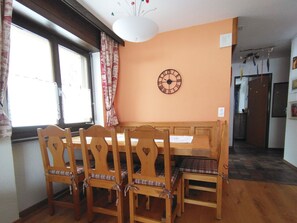Ein Essbereich mit einem Holztisch und Stühlen, einer Wanduhr und einem Fenster mit Vorhängen.