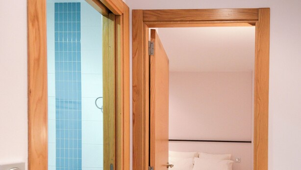 Ein schmaler Flur, der in ein Schlafzimmer mit einem Bett, einem hölzernen Türrahmen und einer blauen Fliesenwand führt.