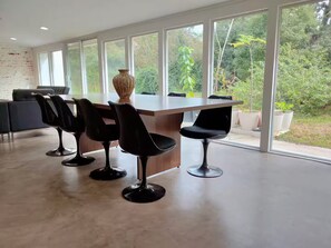 Un espace repas moderne avec une longue table, des chaises noires et un vase.