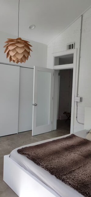 Une chambre à coucher avec un lit, une armoire, une porte et un luminaire au plafond.
