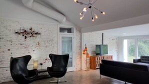 Un soggiorno moderno con una parete in mattoni, un divano in pelle nera, una poltrona in pelle nera, un mobile in legno con televisore e un lampadario di design.
