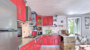 Una cocina con armarios rojos, un refrigerador de acero inoxidable y una encimera de piedra.