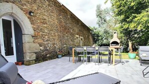 Un patio al aire libre con muros de piedra, un horno de pizza y mobiliario exterior.