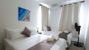 Ein Hotelzimmer mit zwei Betten, einem Gemälde an der Wand, einer Klimaanlage und einem Standventilator.