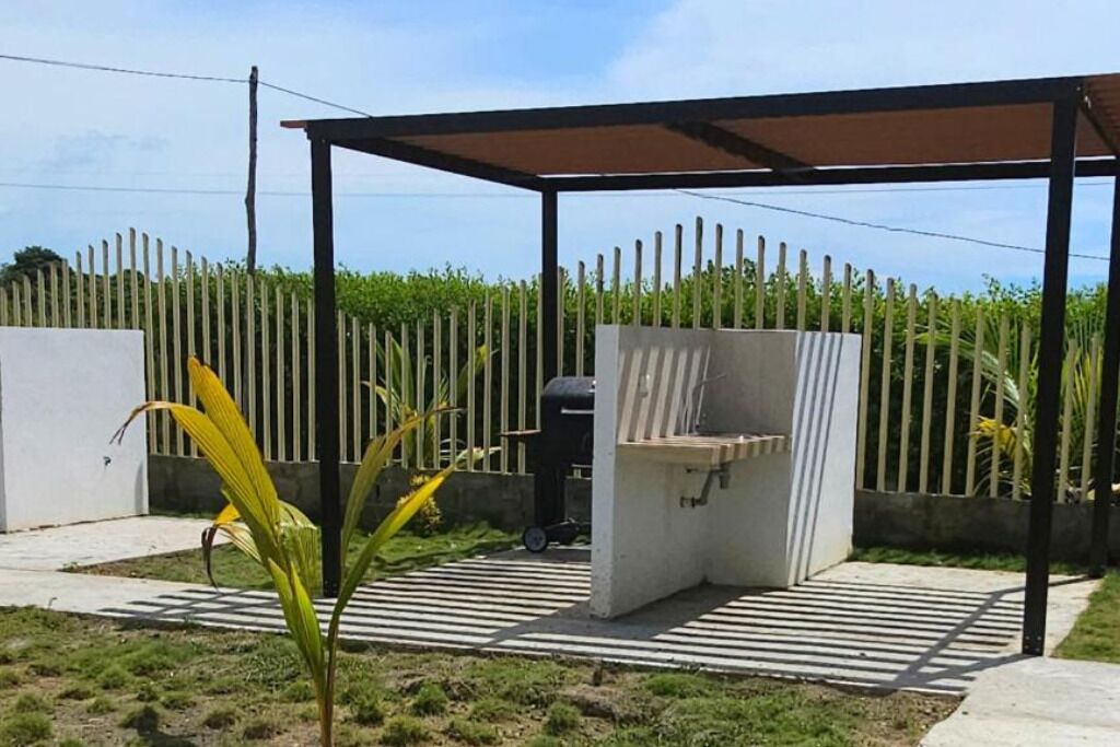 A covered outdoor barbecue area with a grill, a concrete bench, and a striped pathway.