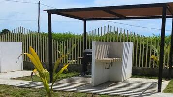 A covered outdoor barbecue area with a grill, a concrete bench, and a striped pathway.