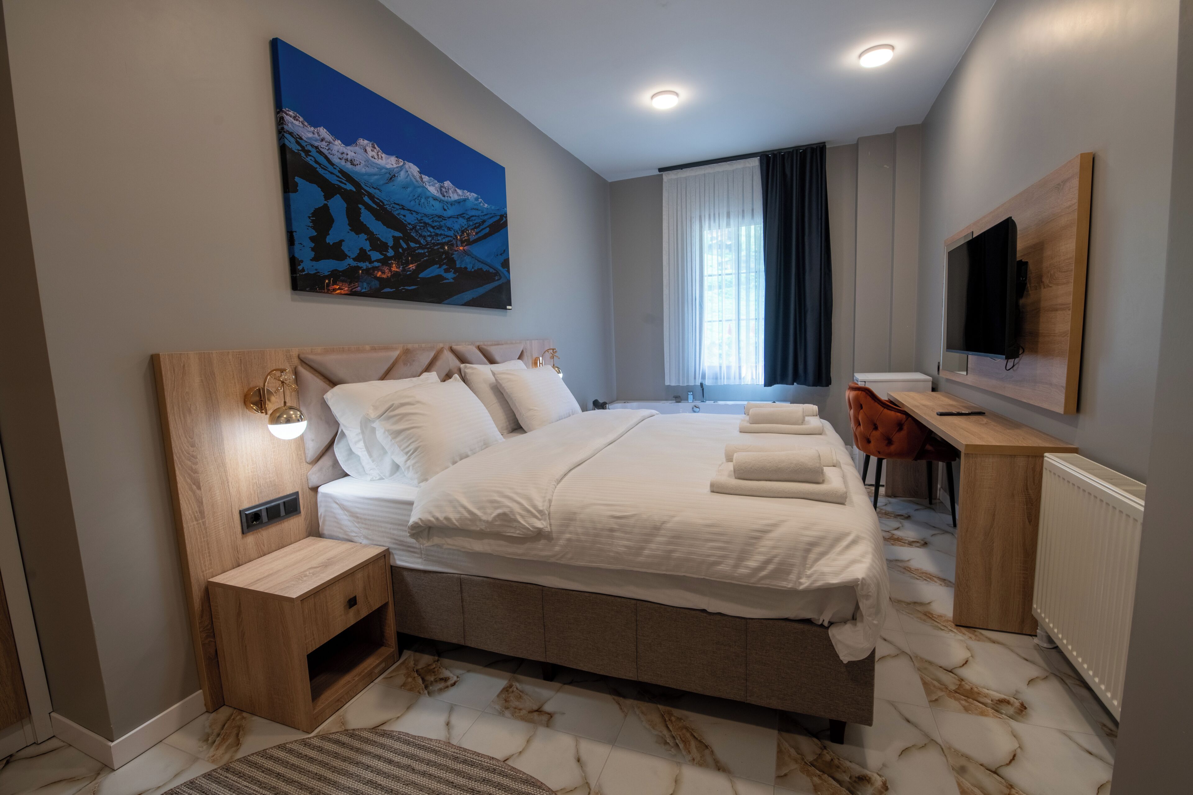 Une chambre d’hôtel moderne avec un grand lit, un bureau, une télévision et un tableau au mur.