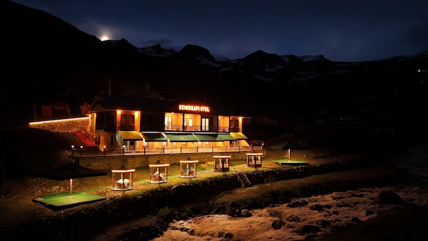 Un hôtel avec une enseigne « HÔTEL DEMIRKAPI » visible la nuit, entouré de montagnes.