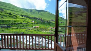Une vue depuis une chambre dotée d’un balcon donnant sur une colline verdoyante, avec une rivière et des maisons.