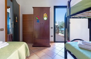 Een kamer met een houten garderobe, een bed, een stapelbed en uitzicht door een glazen deur.