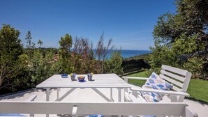 Ett vitt utomhusområde med plats för måltider, komplett med ett bord och bänkar, med en vacker utsikt över havet och kullarna.
