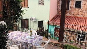 A table set outdoors with a bottle and glass, surrounded by a stone wall and a metal fence. - Acqua del Mare | Welcomely (Tanaunella)