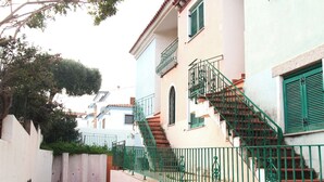 A narrow street with a white building featuring a staircase with green railings and a balcony. - Acqua del Mare | Welcomely (Tanaunella)