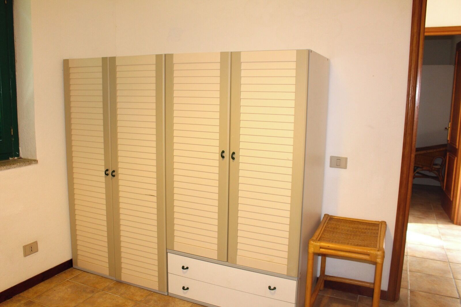Ein Zimmer mit einem großen Kleiderschrank, einem kleinen Holzschemel und einem Fliesenboden.