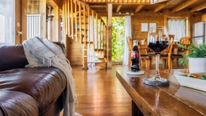 A wooden interior with a leather couch, a dining table with a bottle and glass of red wine, and a staircase leading to an upper level. - Panoramic Views w/ Hot Tub, Pool Table, Arcade! (Sevierville)