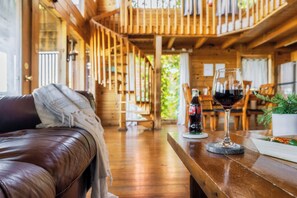 A wooden interior with a leather couch, a dining table with a bottle and glass of red wine, and a staircase leading to an upper level. - Panoramic Views w/ Hot Tub, Pool Table, Arcade! (Sevierville)