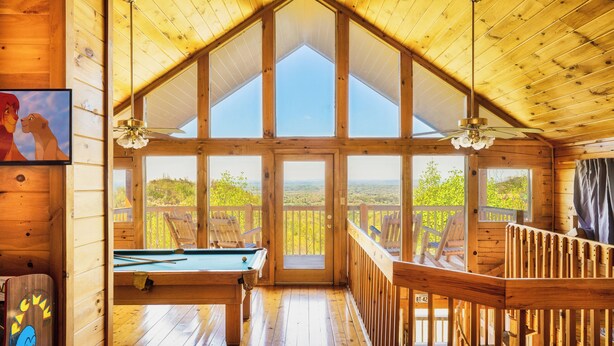 A wooden cabin with a pool table, a ceiling fan, and a view of the outdoors. - Panoramic Views w/ Hot Tub, Pool Table, Arcade! (Sevierville)